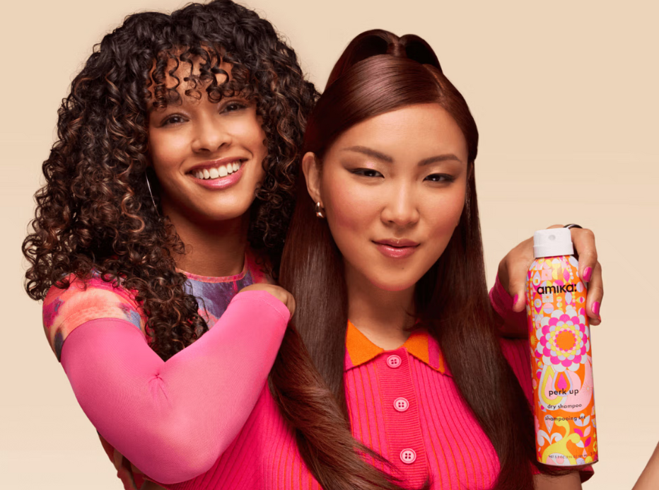 Two women in brightly coloured clothing with different hair textures, one of them holding an Amika product