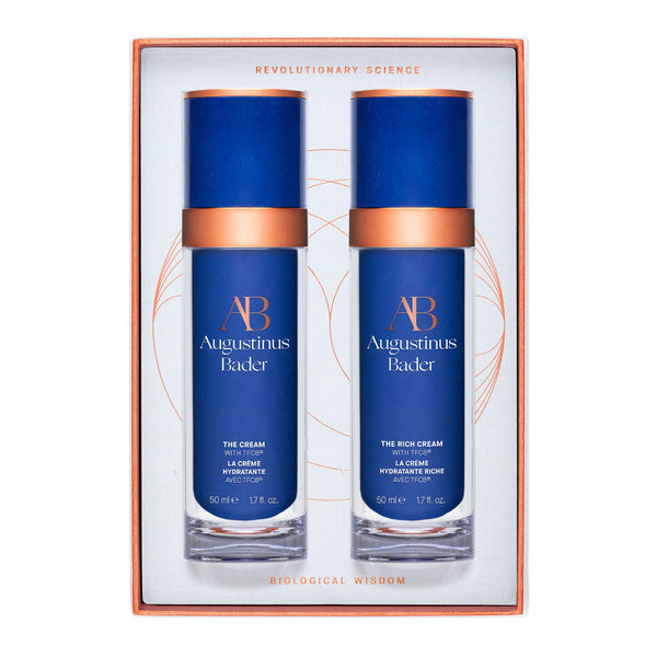 Two blue skincare bottles with bronze accents in a decorative box, featuring the brand 'Augustinus Bader'.