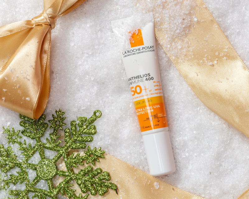 Sunscreen bottle with gold ribbon and green snowflake on a snowy background