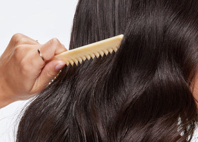 Person combing their wavy hair with a beige comb against a neutral background