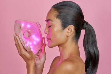 woman holding gold LED face mask to her face