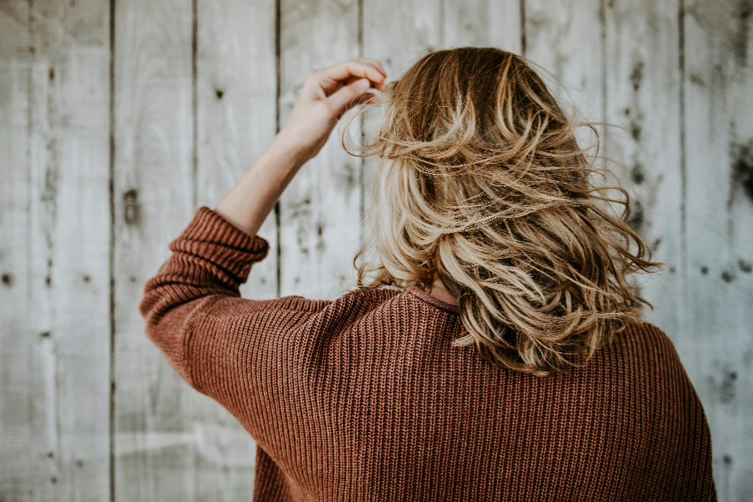 a woman wearing a brown cardi with short blonde hair with her back to the camera