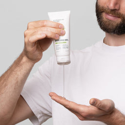 Person holding a tube of styling gel with a clear liquid being dispensed onto their palm.