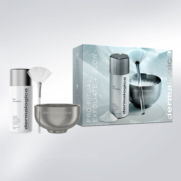 Dermalogica Pro Ritual Exfoliate + Glow gift set featuring a white and silver exfoliating bottle, a metallic bowl, a white fan brush, and the product packaging box on a light gray background.