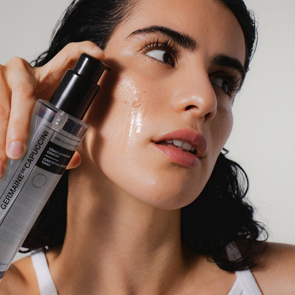 Woman applying a skincare product to her face with a close-up of the bottle.