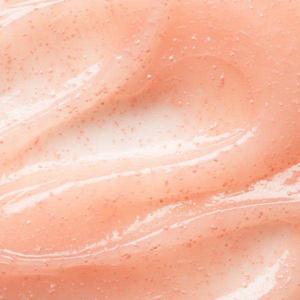 A close-up texture shot of a peach-colored cosmetic gel or cream with fine pinkish-red glitter particles, showing smooth swirls and a glossy finish.