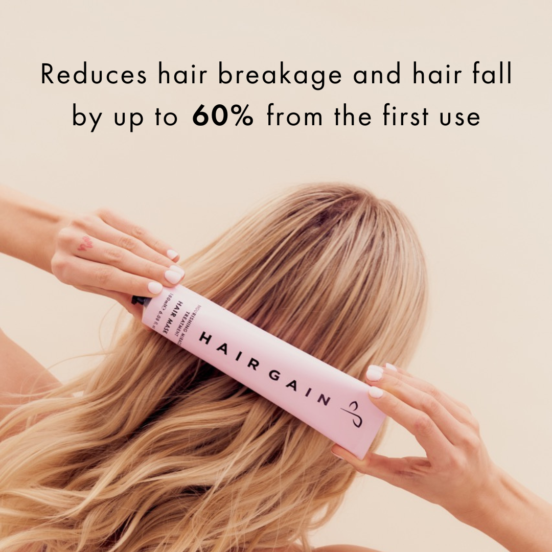 Person holding a pink bottle labeled 'Hairgain' with text about hair care benefits on a beige background