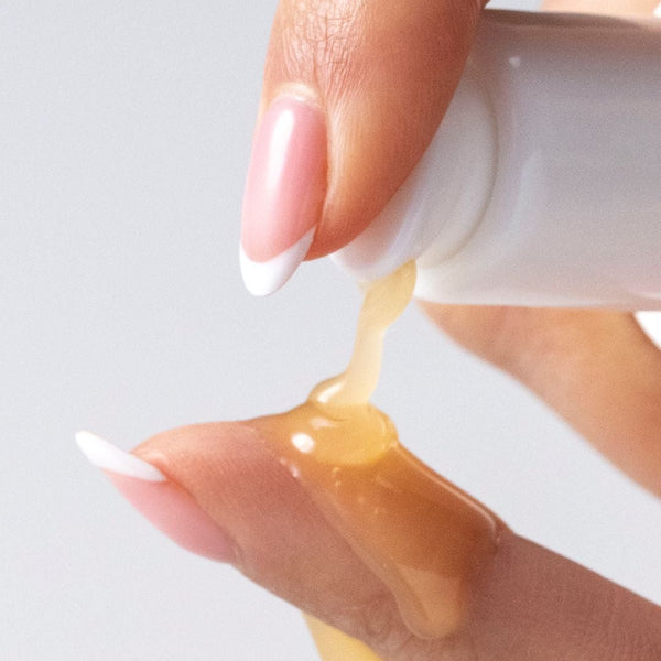 A close-up of a hand dispensing a thick, golden-yellow cosmetic gel or serum onto another finger against a clean, light gray background.