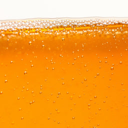 Close-up of a glass filled with orange liquid, likely beer, with bubbles on a white background.