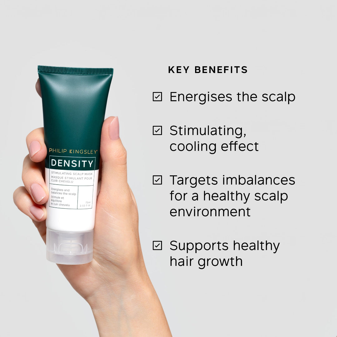Hand holding a tube of Philip Kingsley Density product with key benefits listed on a gray background