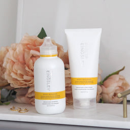 Two bottles of King & Queen skincare products on a marble surface with flowers in the background.