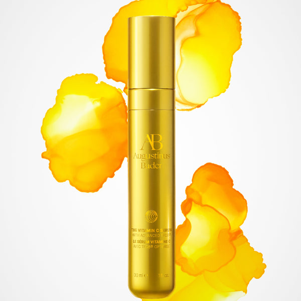 Gold skincare bottle with 'AB' branding on a white background with yellow floral elements