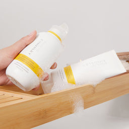 Hand holding a bottle of Arbonne product with a tube on a wooden tray.