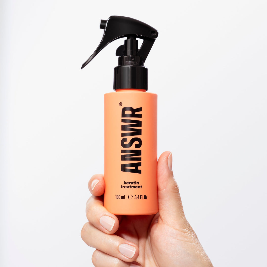 Hand holding an orange bottle with a black sprayer labeled 'ANSWR' against a white background