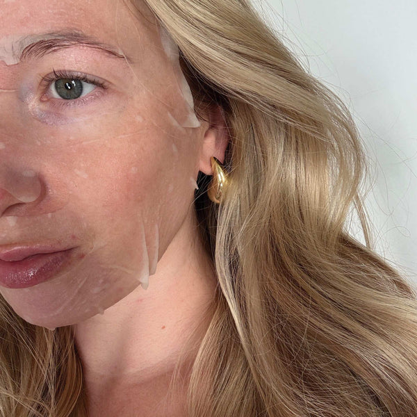 Close-up of a woman with blonde hair and a gold earring, showing a before-and-after effect on her skin.
