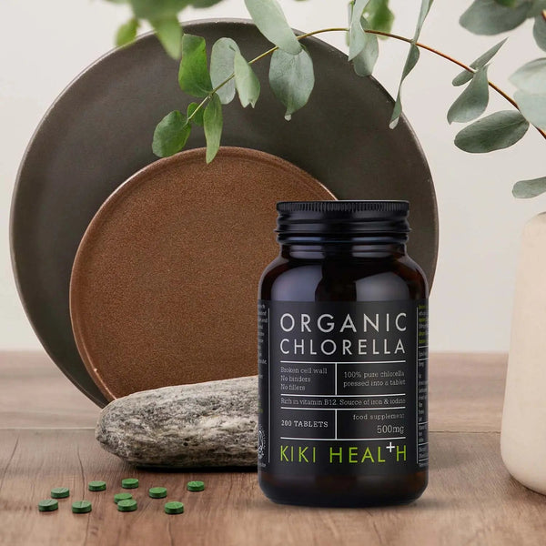 Kiki Health Organic Chlorella supplement bottle on a wooden surface with decorative elements.