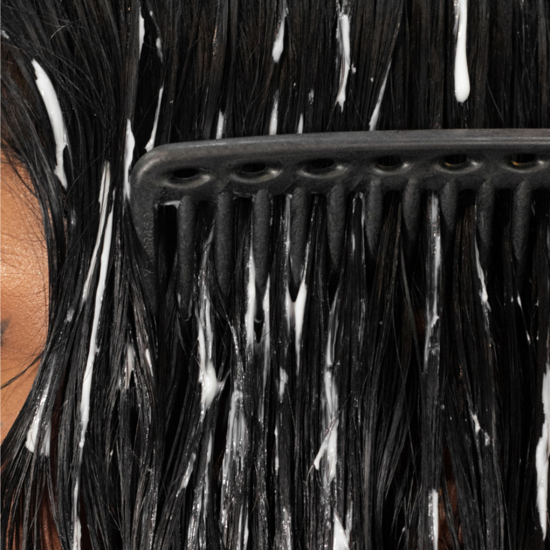 Close-up of a comb through wet hair with white conditioner or shampoo being applied.