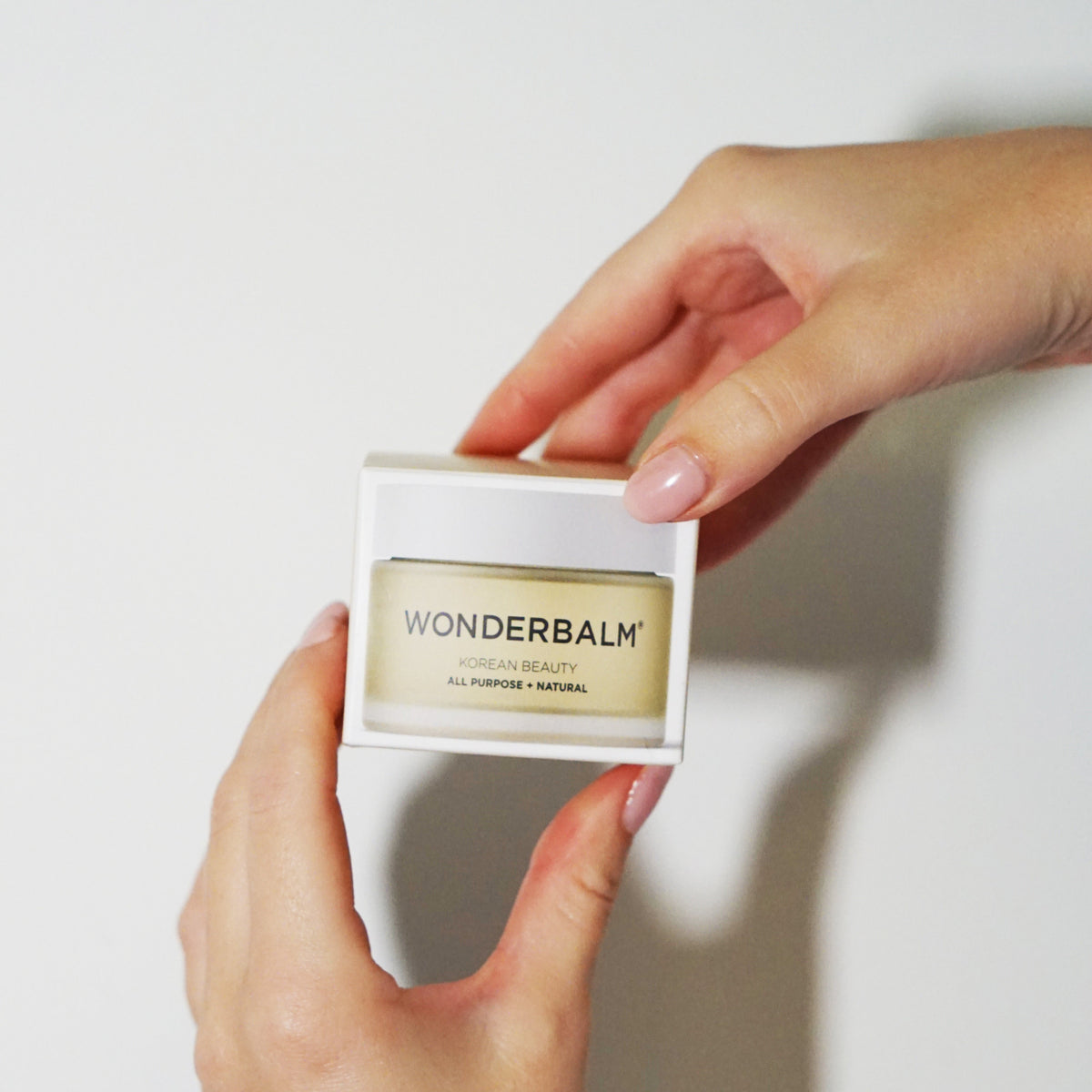 Person holding a small container of Wonderbalm against a plain background