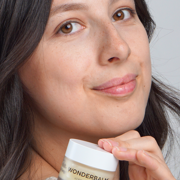 Woman holding a jar of Wonderbalm against a neutral background