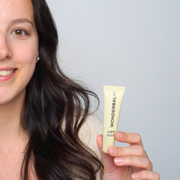 Woman holding a Wonderbalm lip balm against a plain background