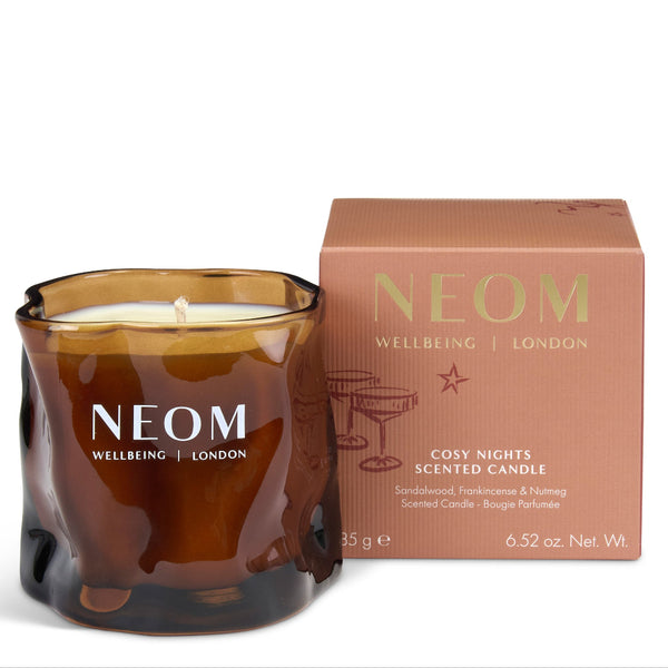 NEOM Cosy Nights scented candle in a textured amber glass jar next to its dusty rose packaging box, on a clean white background.