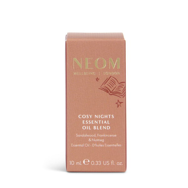 A rectangular pinkish-rose box of NEOM Cosy Nights Essential Oil Blend on a clean white background. The box features gold and white text with a small illustration of an open book and stars.