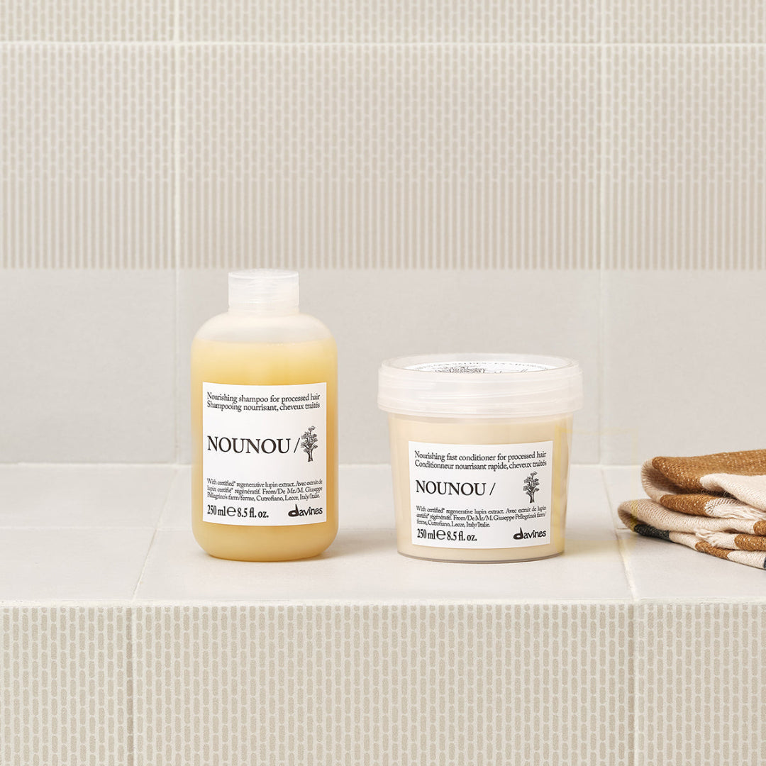 Two bottles of NOUNOU hair care products on a bathroom shelf with a tiled wall background.