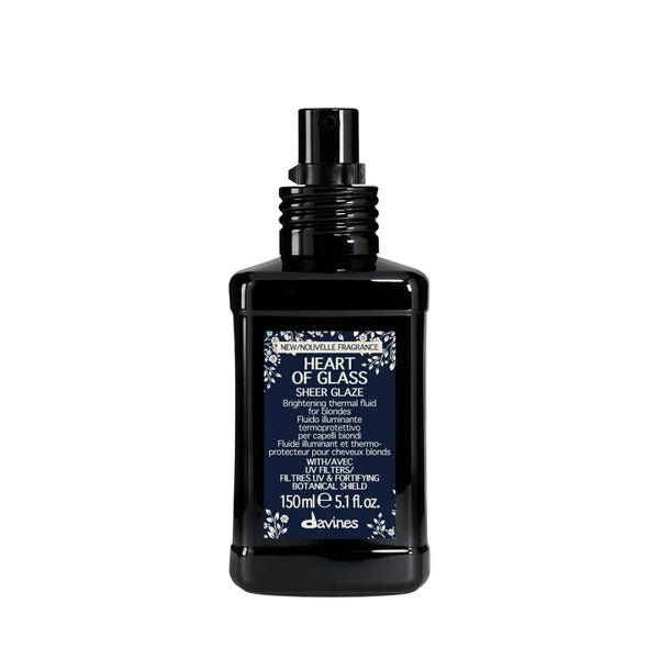 A black bottle of Davines Heart of Glass Sheer Glaze with a matching black spray nozzle, featuring a navy blue label with white text and floral borders, set against a plain white background.