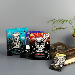 Collection of Barber Pro eye mask packages on a gray surface with a plant and books in the background.