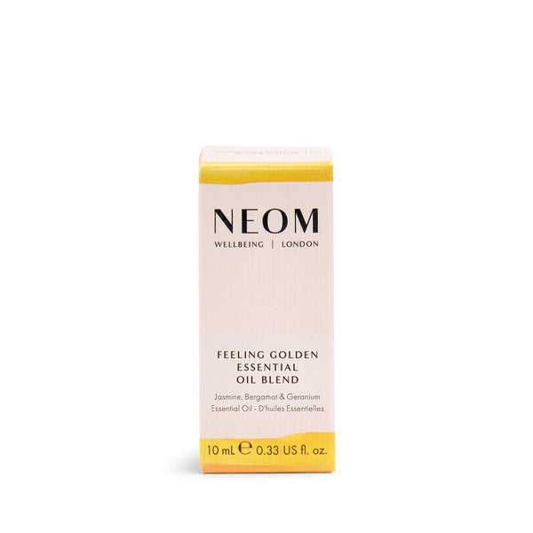A 10 mL box of NEOM Wellbeing 'Feeling Golden' Essential Oil Blend, featuring a pale pinkish-beige box with yellow bands at the top and bottom, and black text.