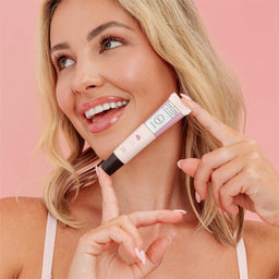 Woman holding a cosmetic product against a pink background