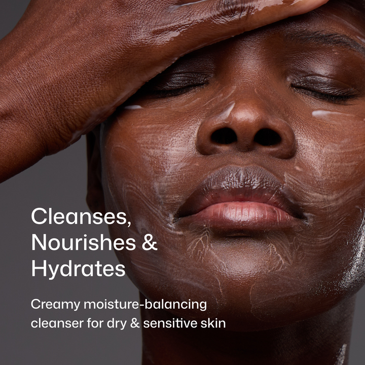 Close-up of a person with a dark complexion applying or wearing a creamy skincare cleanser, with text reading 'Cleanses, Nourishes & Hydrates' and 'Creamy moisture-balancing cleanser for dry & sensitive skin' on a dark gray background.