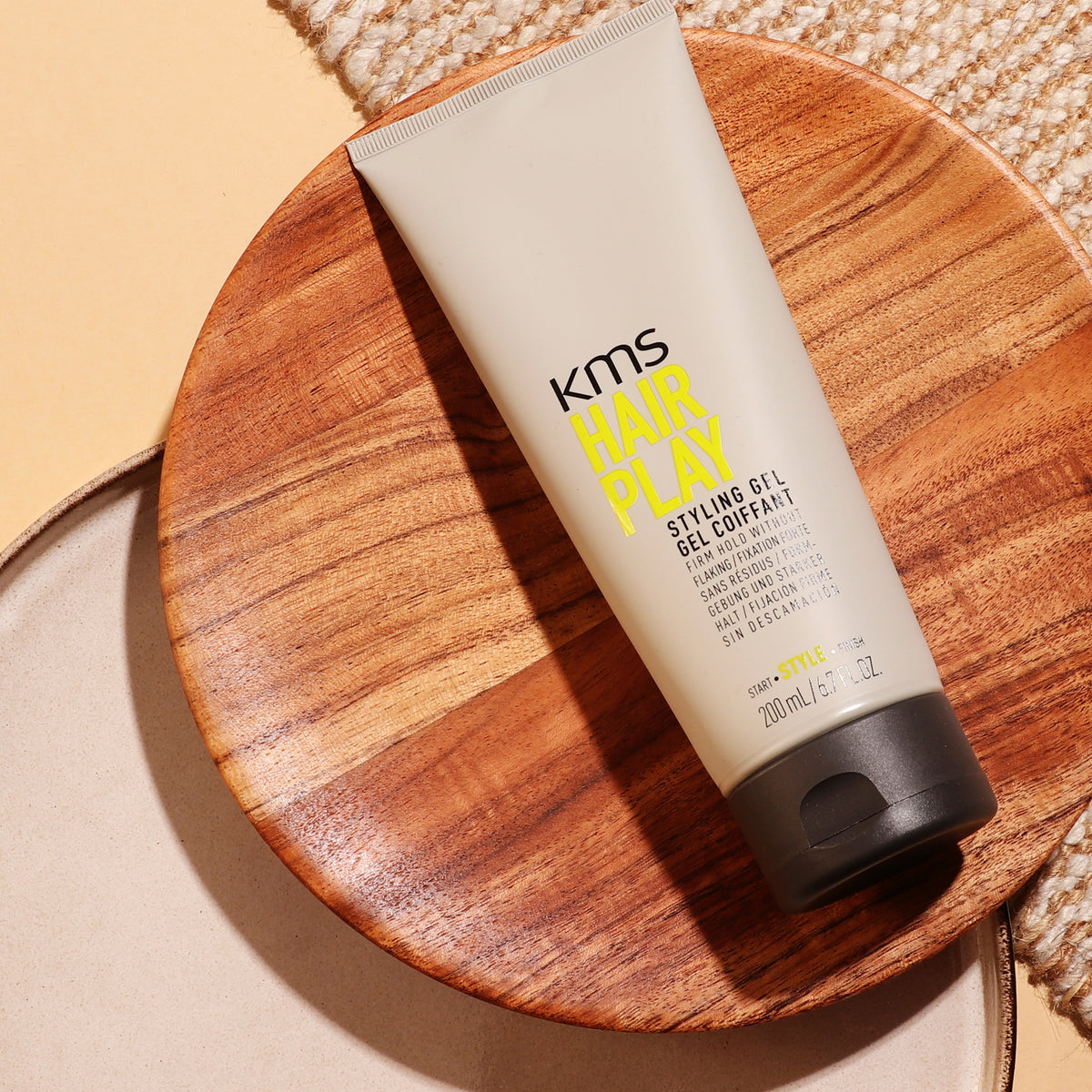 KMS Hair Play styling gel on a wooden plate with a neutral background
