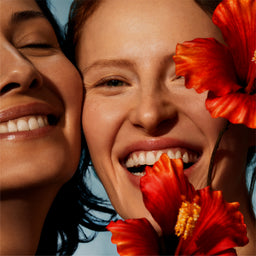 Two women smiling with red flowers in the foreground