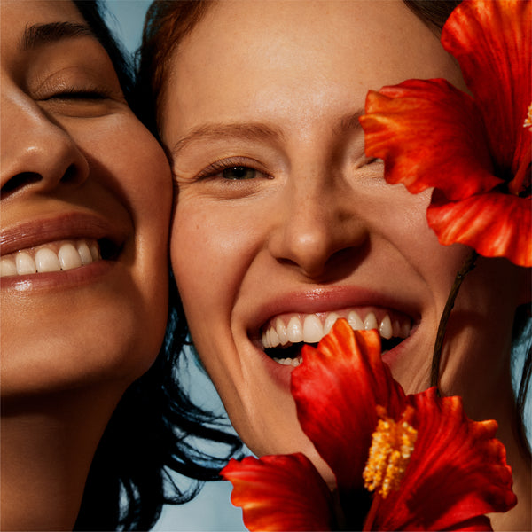 Two women smiling with red flowers in the foreground