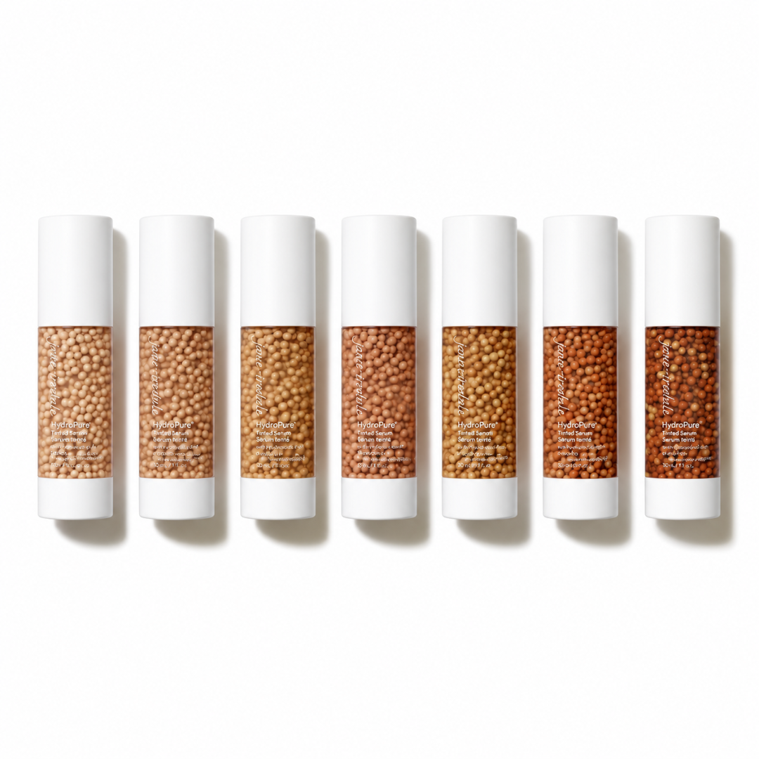 Six white cosmetic tubes arranged in a row on a white background, each showing a different shade of tan and brown seed beads in the clear center window.