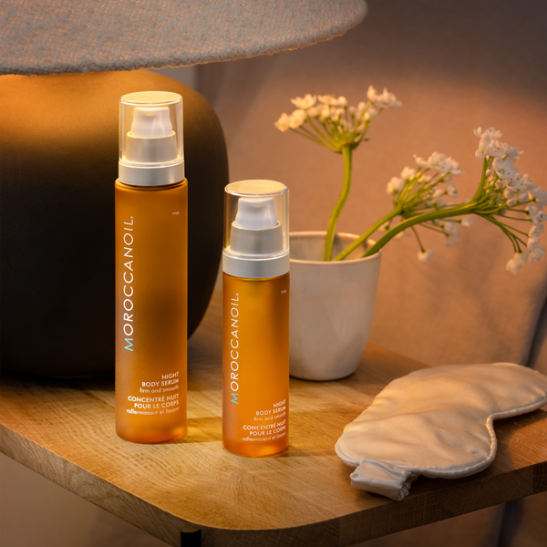 Two bottles of Moroccanoil product on a wooden surface with a plant in the background.