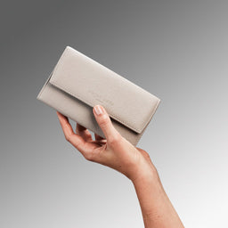 Hand holding a beige clutch against a gray background