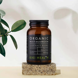Brown bottle of Organic Multi-Mushroom 8 Extract Blend by KIKI Health on a light background with a plant.