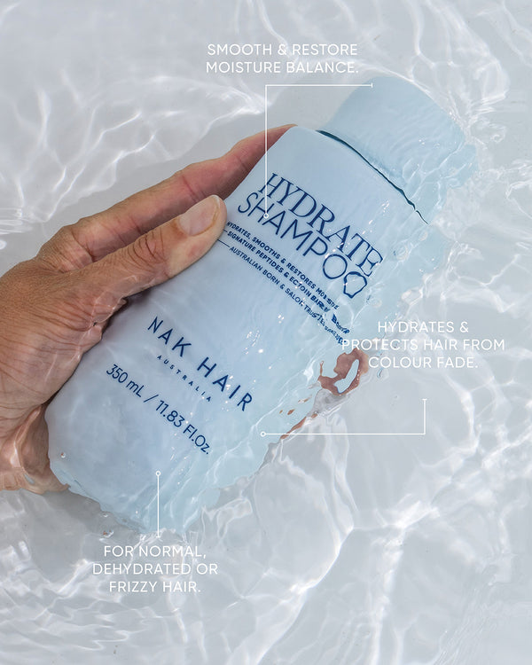 Hand holding a bottle of NAK Hair Hydrate Shampoo against a light background