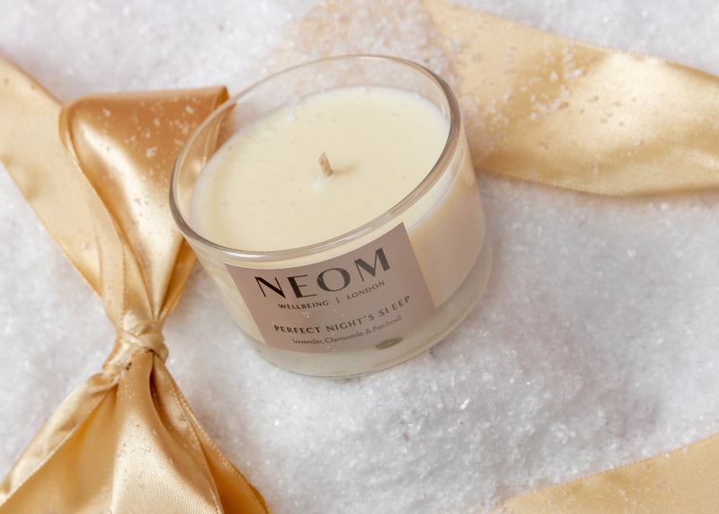 Neom candle with gold ribbon and green snowflake on white background