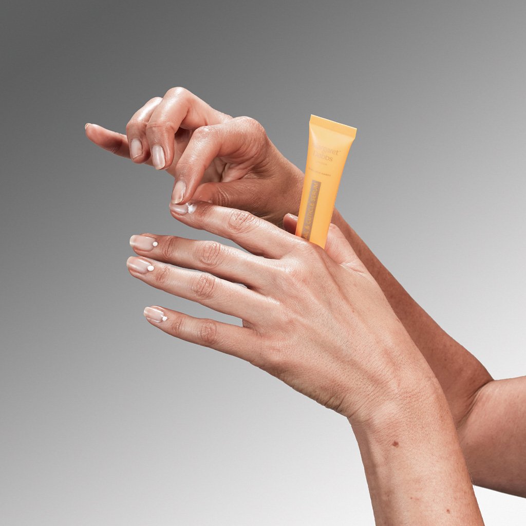 Hand applying a small tube of cream on a gray background
