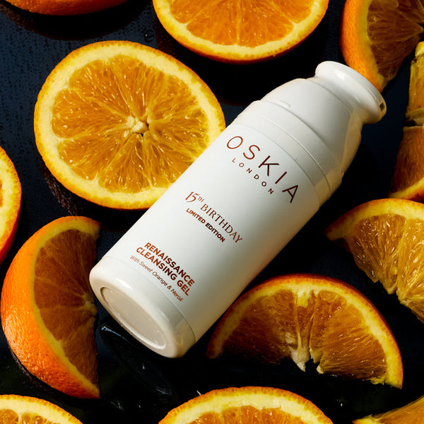 OSKIA skincare bottle surrounded by sliced oranges on a dark surface