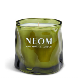 A green glass jar candle with a wavy, organic shape and a single wick, featuring the white text 'NEOM WELLBEING | LONDON' on the front, set against a plain white background.