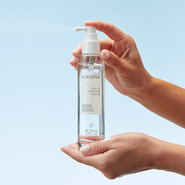 Hand holding a Kerastik hair care product bottle against a light blue background