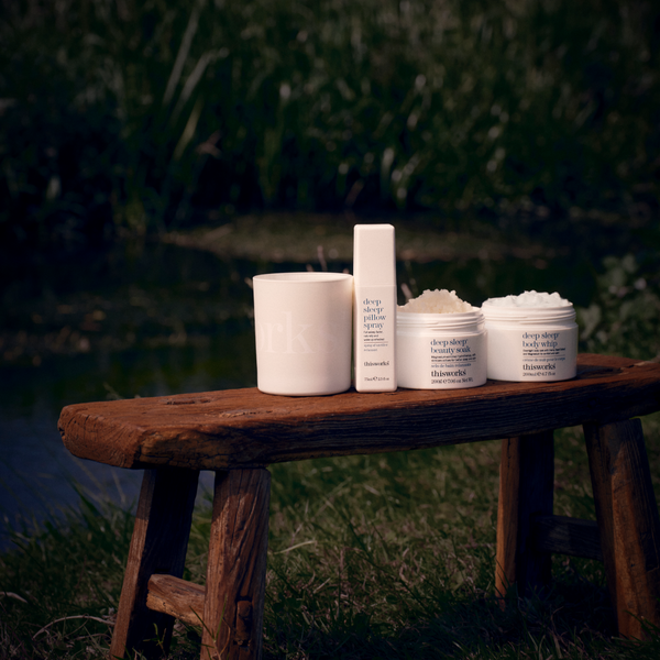 Four skincare products from deep-drip beauty by Dr. Lipp are arranged on a rustic wooden bench outdoors near grass and water.