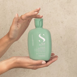 Person holding a green bottle of Alfaparf Milano styling product against a beige background