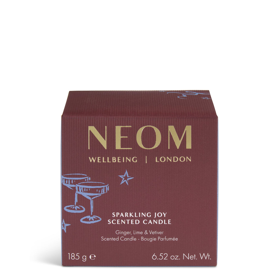 A square NEOM Wellbeing London scented candle box in a deep burgundy color with gold lettering and light blue line-art illustrations of cocktail glasses and stars, shown on a clean white background.