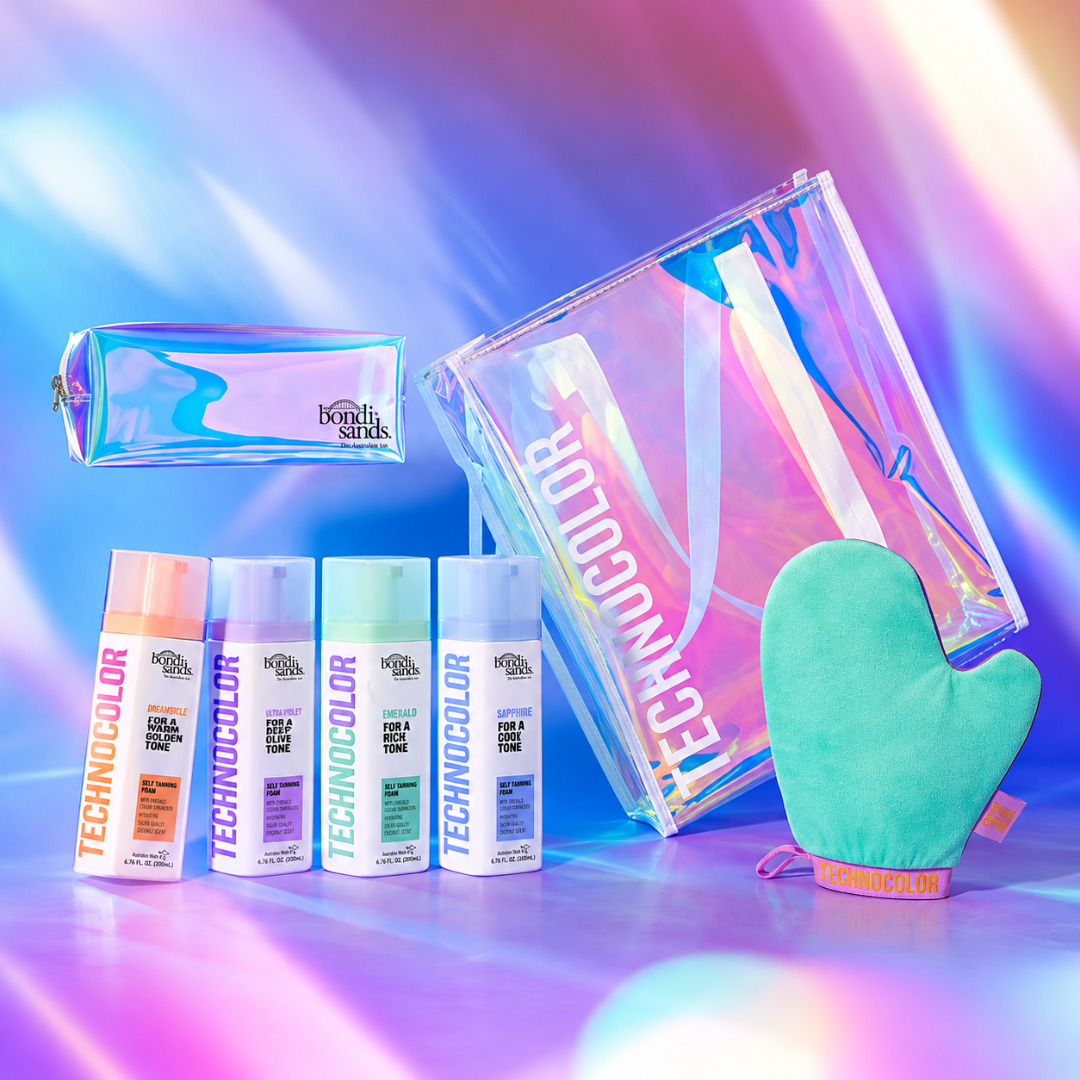 A Technocolor haircare gift set featuring four bottles of hair color, a holographic zip pouch, a larger holographic cosmetic bag, and a mint green silicone oven mitt, arranged on a vibrant, iridescent purple and blue background.