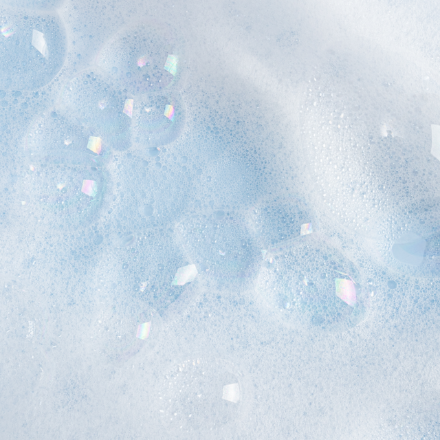 A close-up of pale blue and white foamy texture with translucent bubbles and scattered iridescent square pieces.